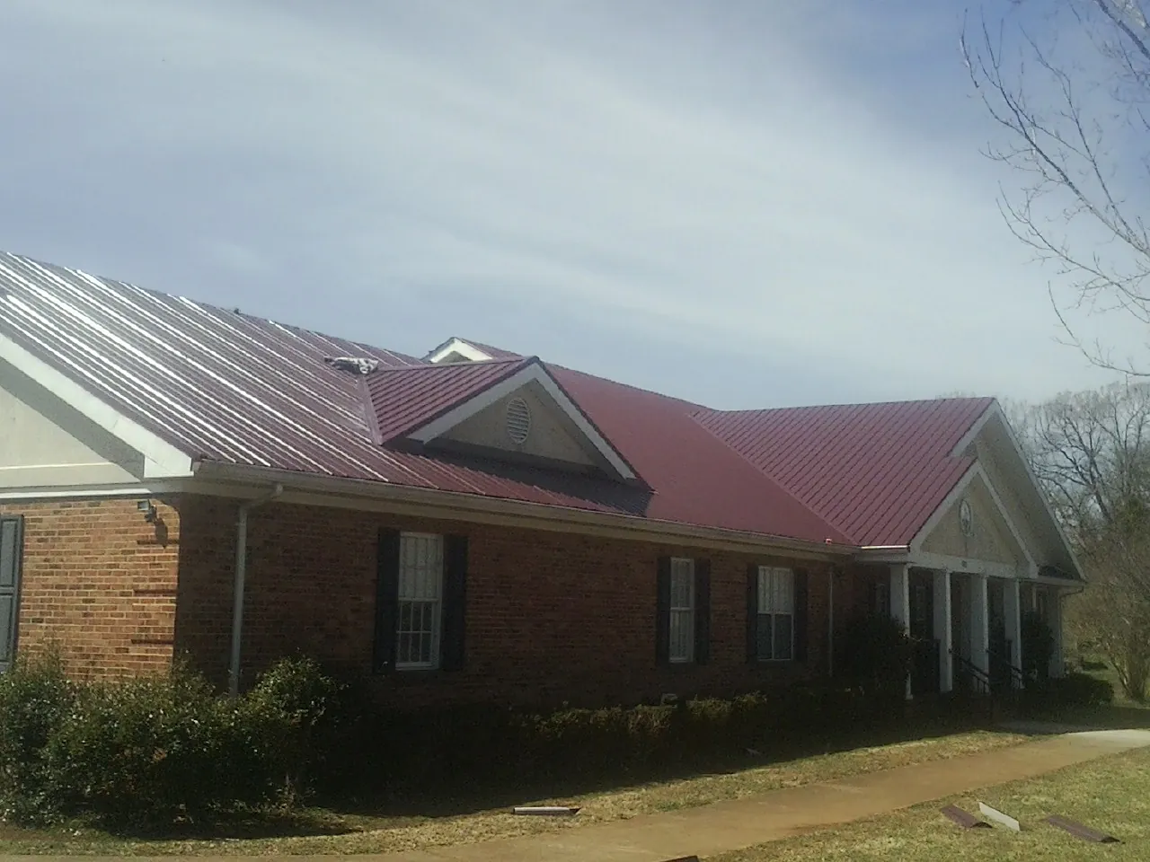Red metal roof with gabled entries on a long brick building, from a Hail Damage Roof Repair job in East Ellijay
