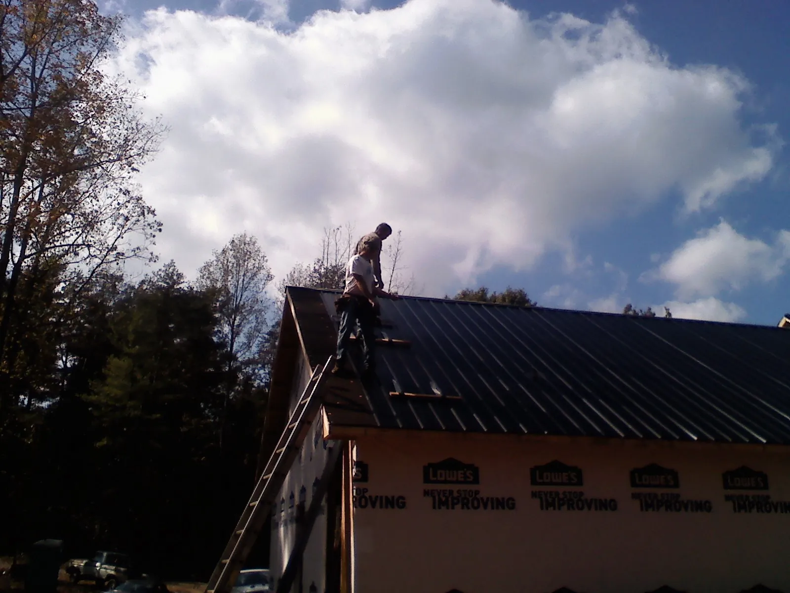 Roofer fastening dark metal panels high against a cloudy sky, from a Roof Inspection job in East Ellijay