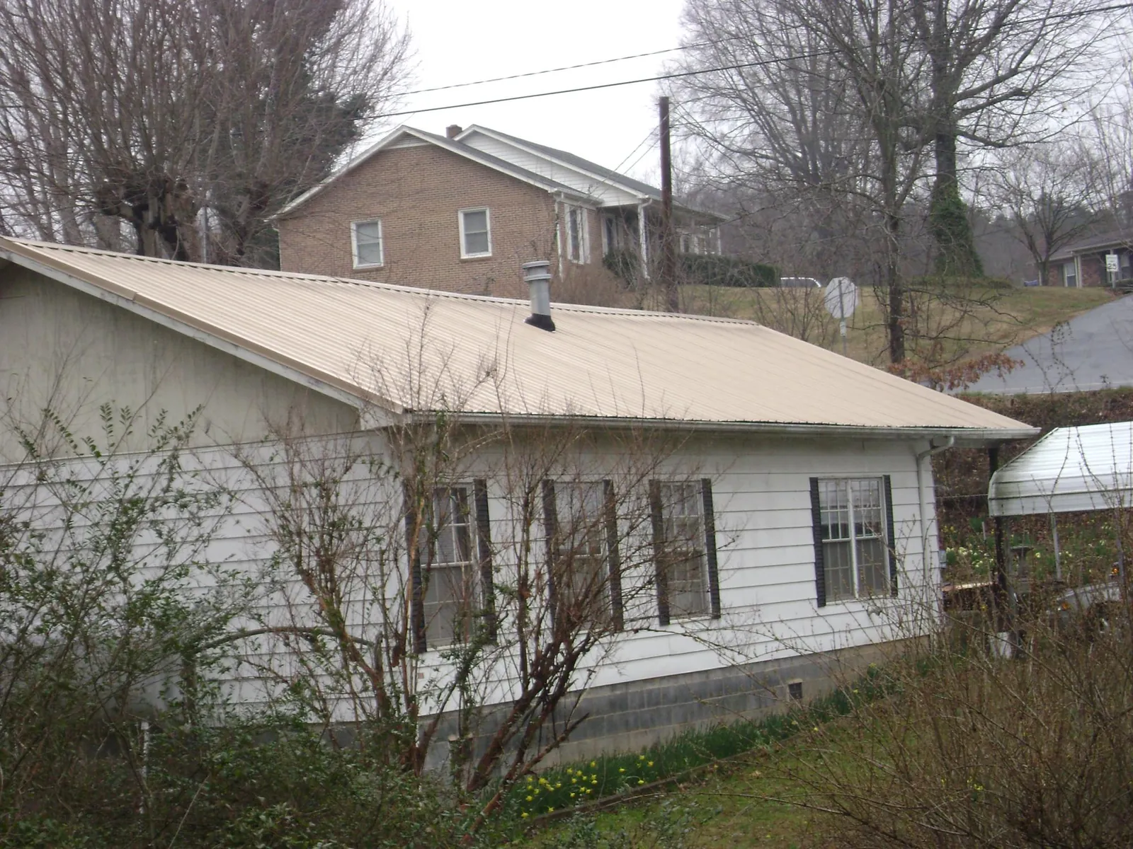 Tan metal roof on a white sided house set into a hillside — Commercial Roofing by Roofing Brothers in East Ellijay